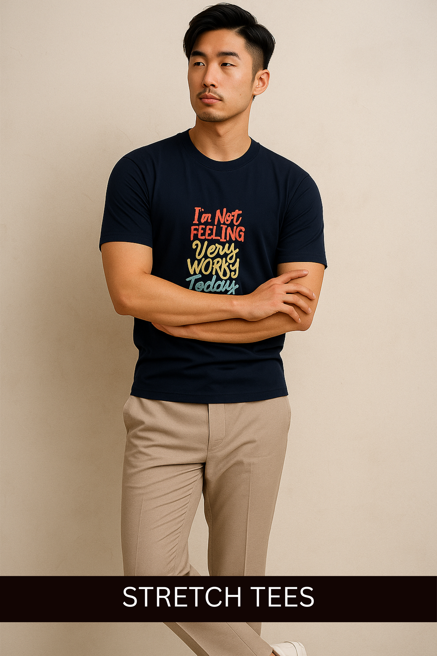 Man wearing a navy men's stretch t-shirts with colorful text graphic and beige pants standing against a neutral background