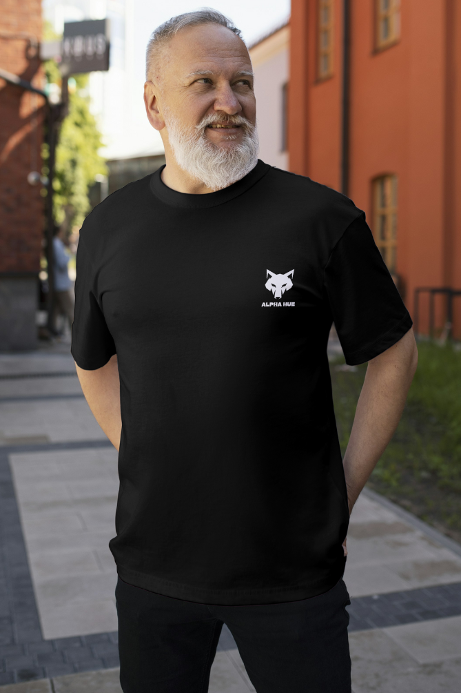 Men's oversized graphic t-shirt in black with Alpha Hue logo worn by smiling bearded man outdoors